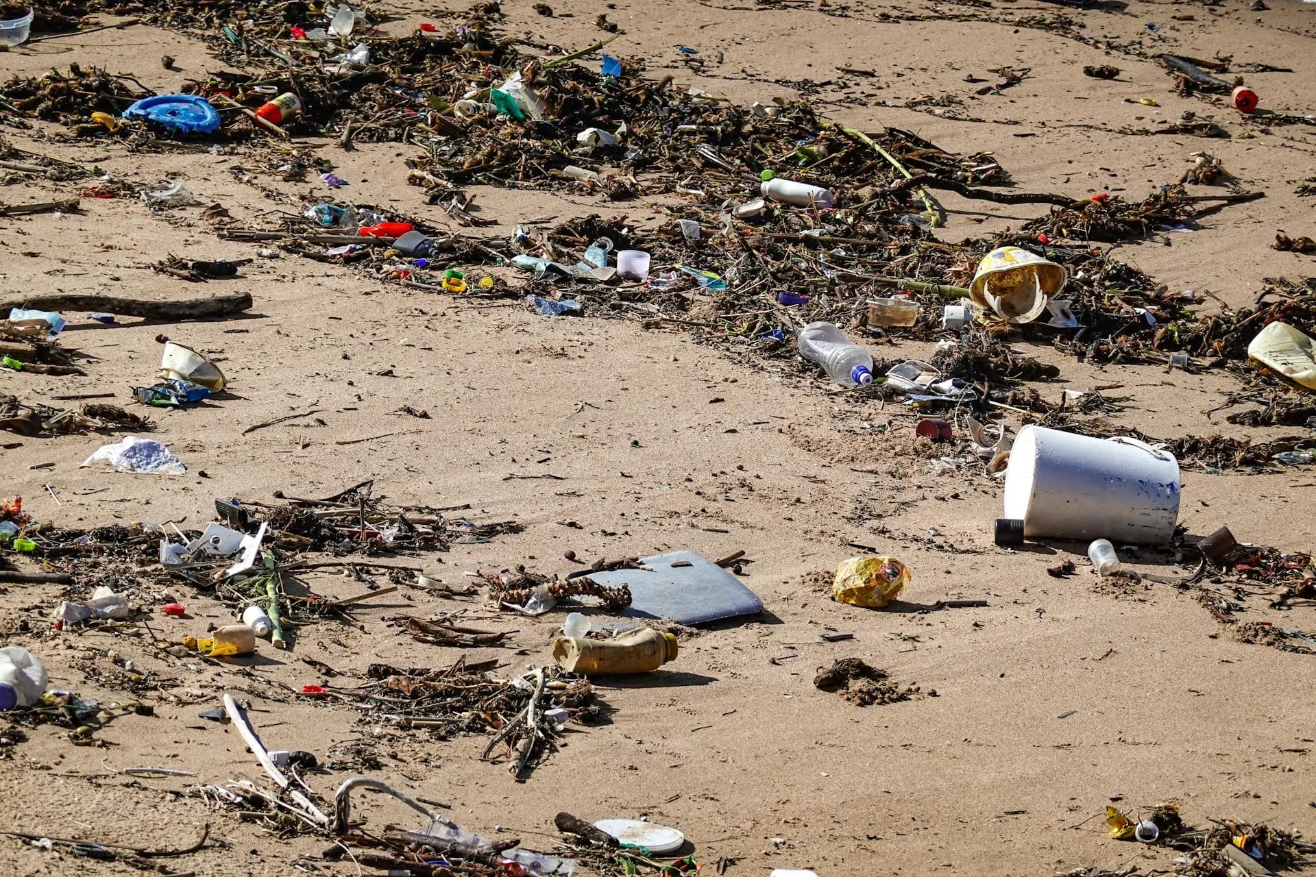 Plastic waste and debris littered across a sandy beach shore.