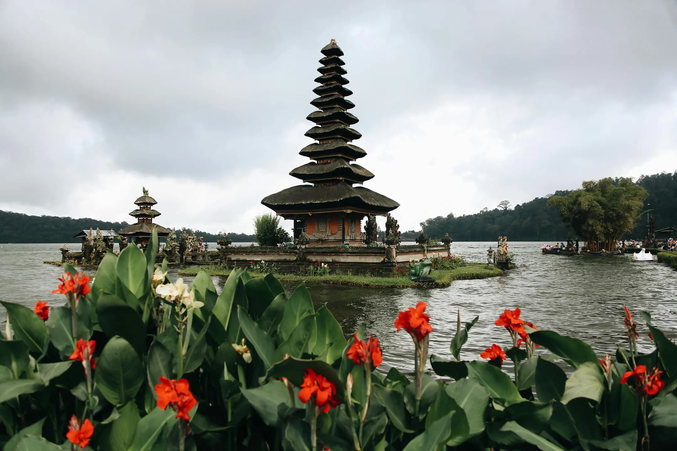 An image of the Ulun Danu Beratan Temple in Bali depicts a serene lakeside surrounded by lush greenery and vibrant red flowers in the foreground.